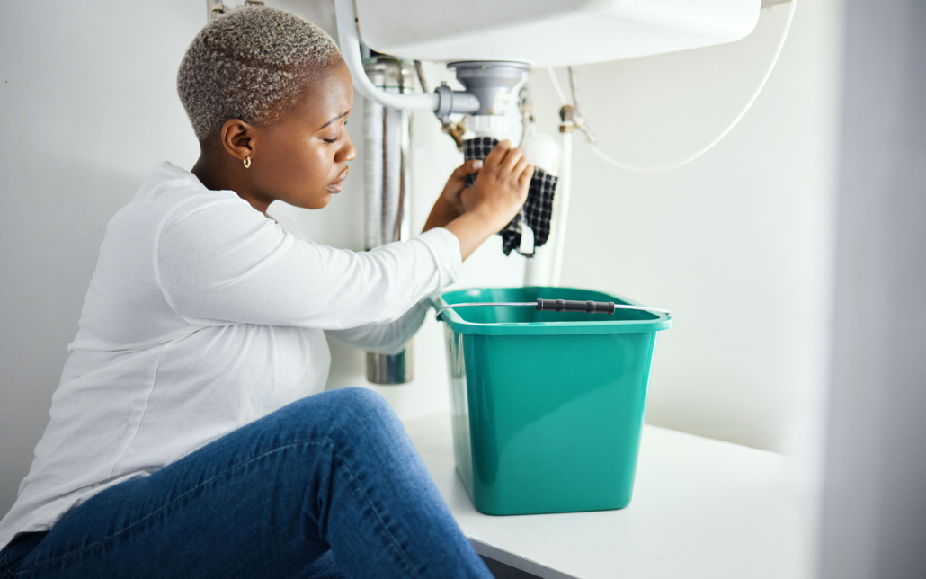 Side view of a woman sitting on her bathroom floor wiping off a burst pipe